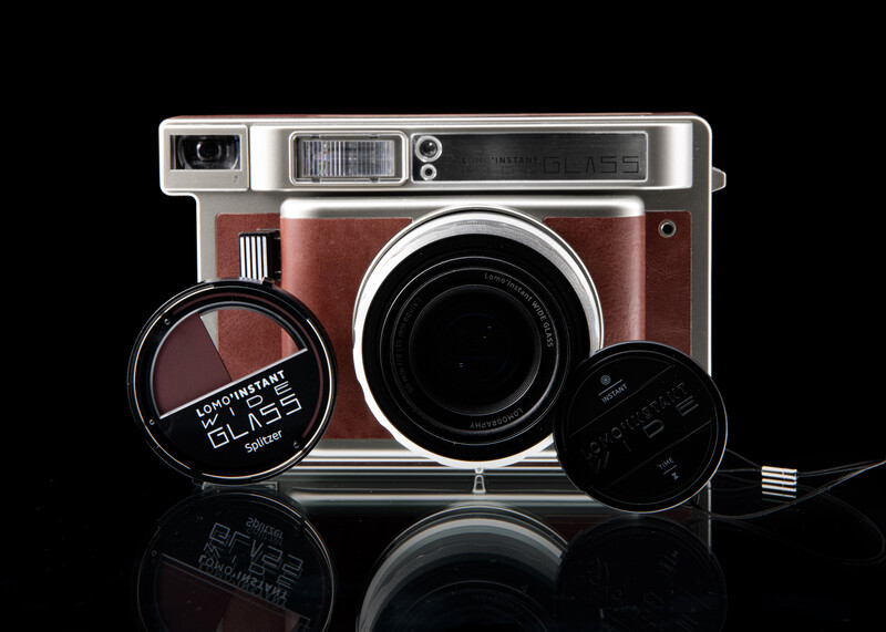 Fisheye instant film camera in brown leather with detachable lens and accessories on black background.