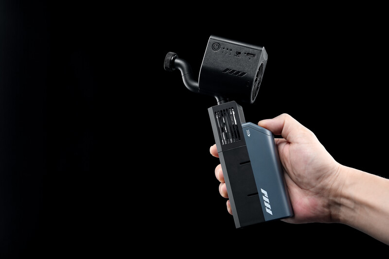 Hand holding a wireless flash trigger transmitter with a flash unit mounted above against a black background.