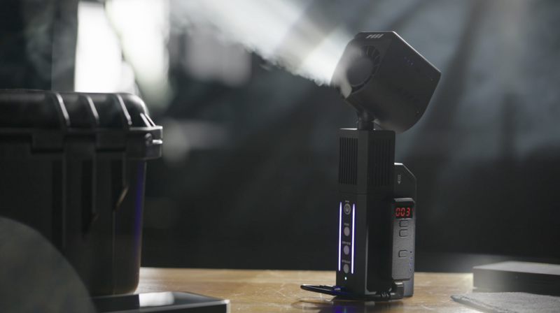 Professional lighting setup with a compact LED panel mounted on a stand, emitting bright white light with visible dust particles in the beam.