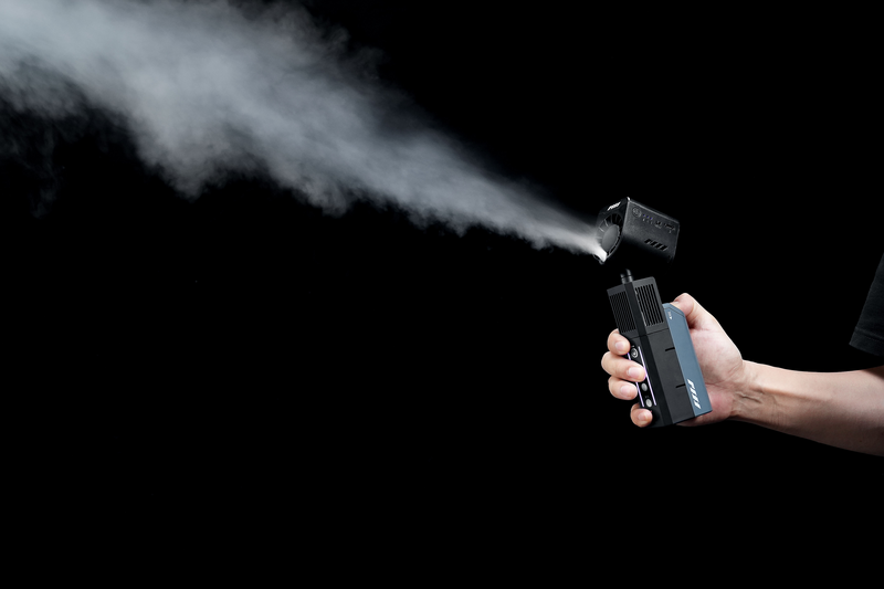 Hand holding a compact spray device spraying mist against a black background.