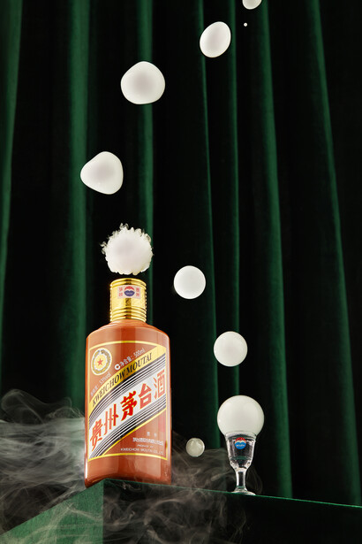Liquor bottle with floating spheres and glass, surrounded by green velvet and dry ice fog.