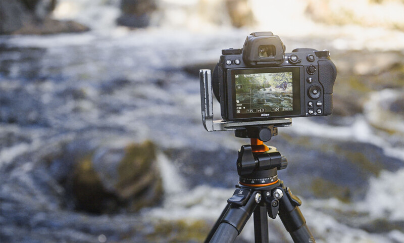 Mirrorless camera mounted on tripod with L-bracket, displaying river landscape on rear screen.