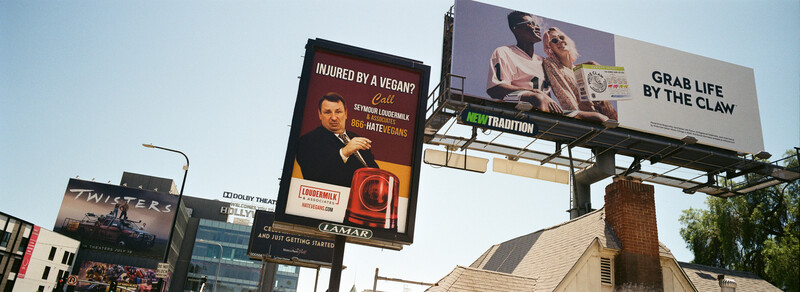 Multiple billboards along an urban street displaying various advertisements against a clear sky.