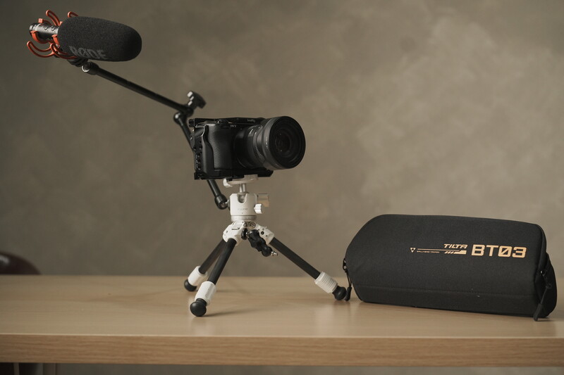 Compact camera rig with telephoto lens, shotgun microphone, and tripod on wooden surface.