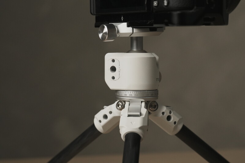 White ball head with dual friction arms mounted on black tripod legs with camera above.