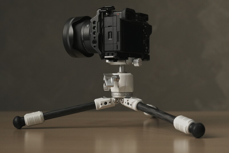 Mirrorless camera mounted on a white ball head and tripod with black legs against a neutral background.