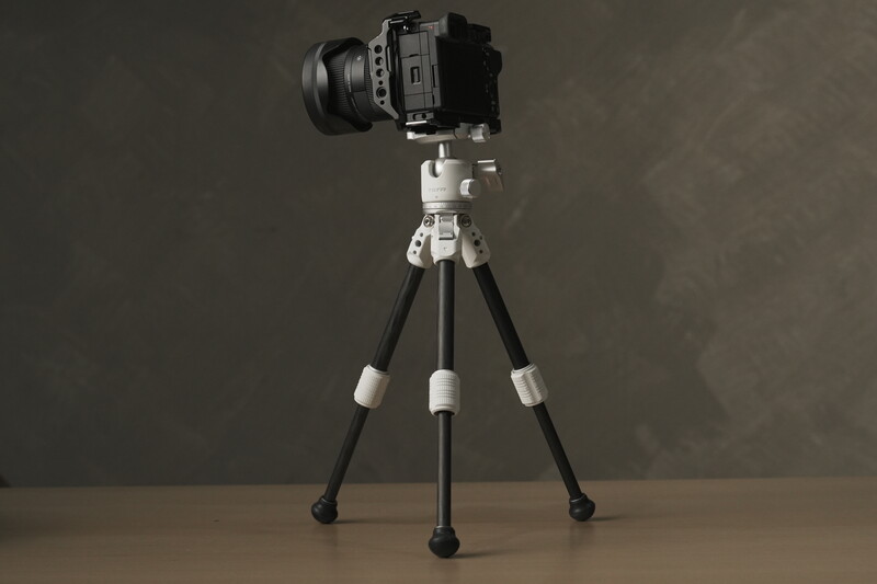 Mirrorless camera with wide-angle lens mounted on a compact tripod with black legs and white joints.