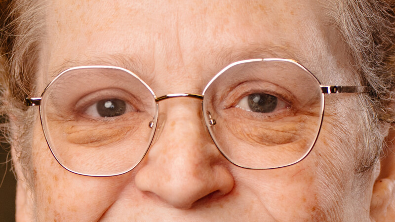 Close-up portrait of an older man wearing wire-rimmed glasses with a neutral expression.