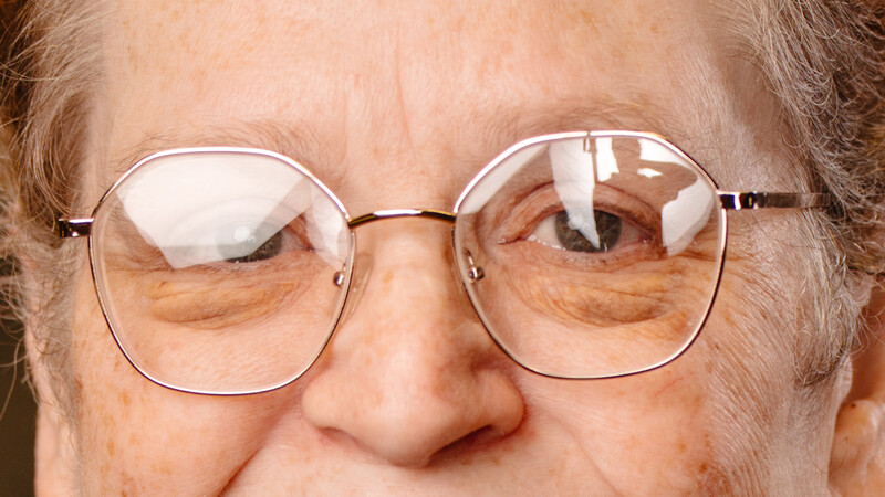 Close-up of an older man wearing metal-framed eyeglasses with reflective lenses.