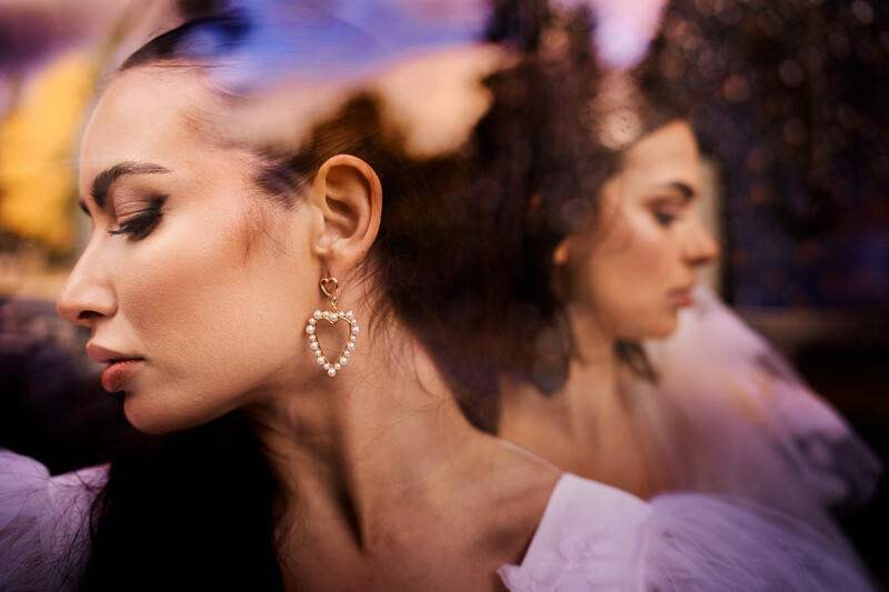 Woman in profile wearing heart-shaped diamond earrings with soft, warm lighting and blurred background.