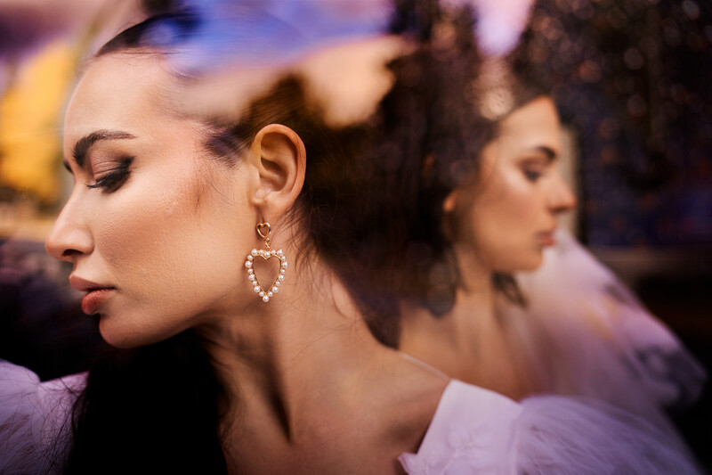 Woman in profile with closed eyes wearing heart-shaped diamond earrings, soft warm and cool lighting.