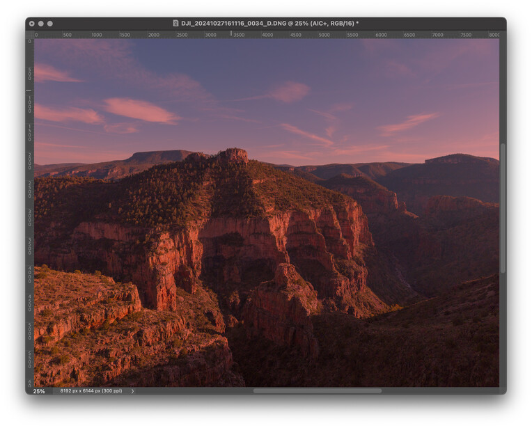 Dramatic canyon landscape at sunset with golden-lit cliff faces under purple and pink sky.