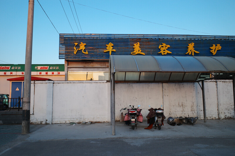 Weathered storefront with golden Chinese characters on blue corrugated metal awning, parked motorcycles in foreground.