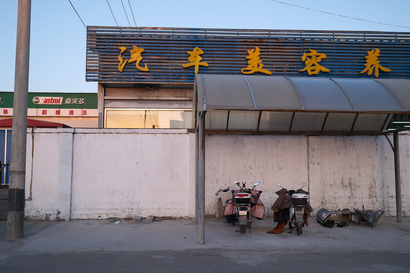 Shuttered storefront with Chinese characters on signage and parked motorcycles beneath a covered awning.