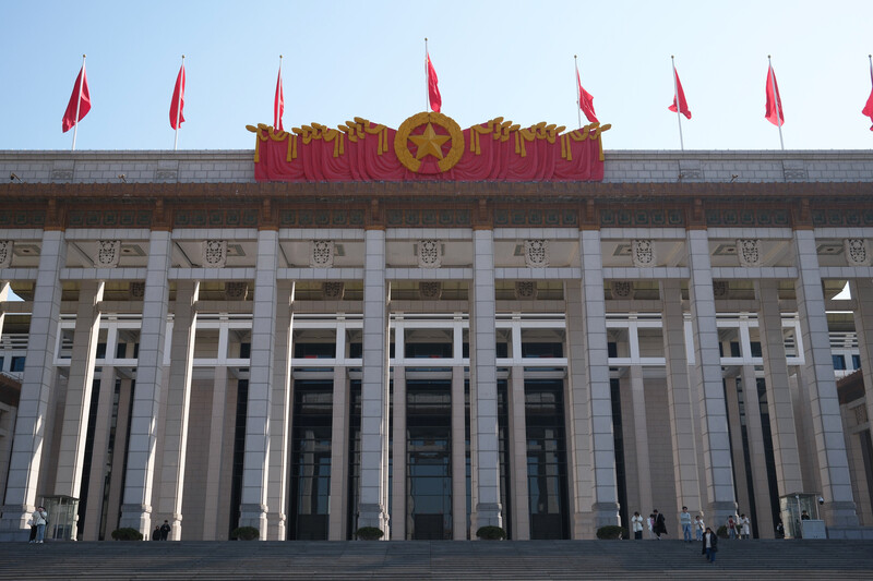 Monumental government building with classical columns and red flags bearing a gold star emblem on the roofline.