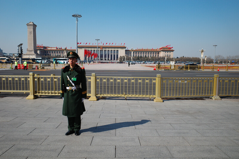 Uniformed guard standing alone on a vast plaza with a grand government building in the background.