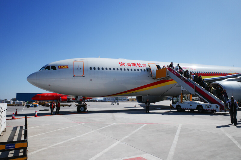 Large commercial aircraft parked at airport terminal with passengers boarding via stairs in bright daylight.