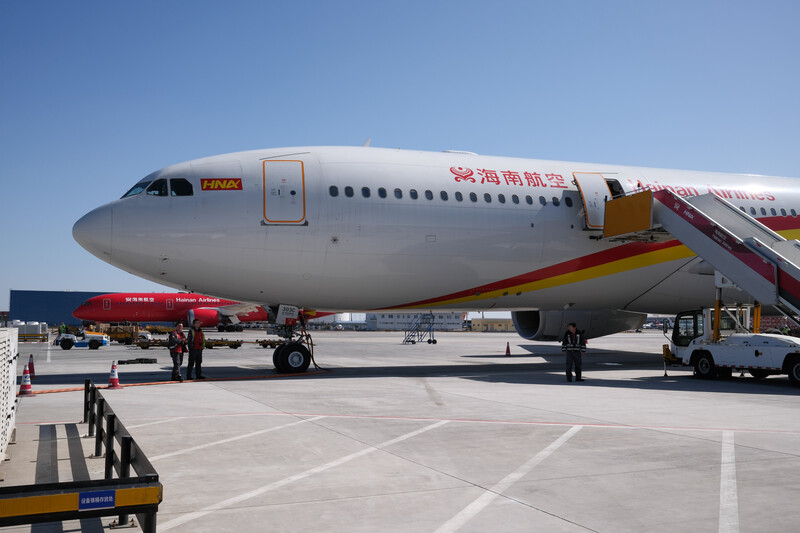 Wide-body commercial aircraft parked at airport gate with boarding stairs and ground vehicles.