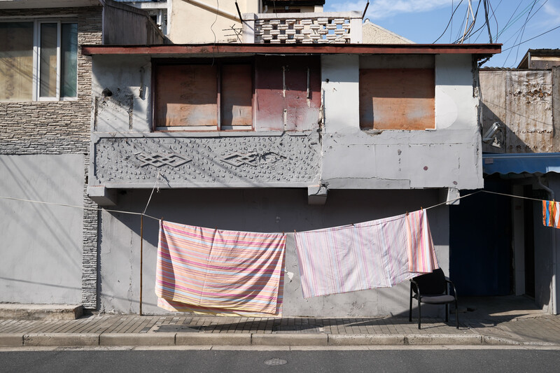 Weathered two-story residential building with boarded windows and pink striped laundry hanging on clothesline.