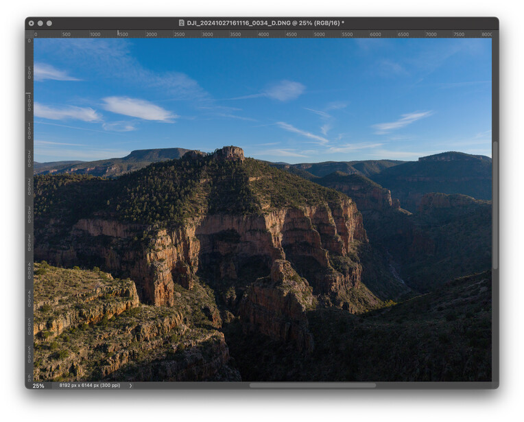 Rugged canyon landscape with layered rock formations and forested slopes under clear blue sky.