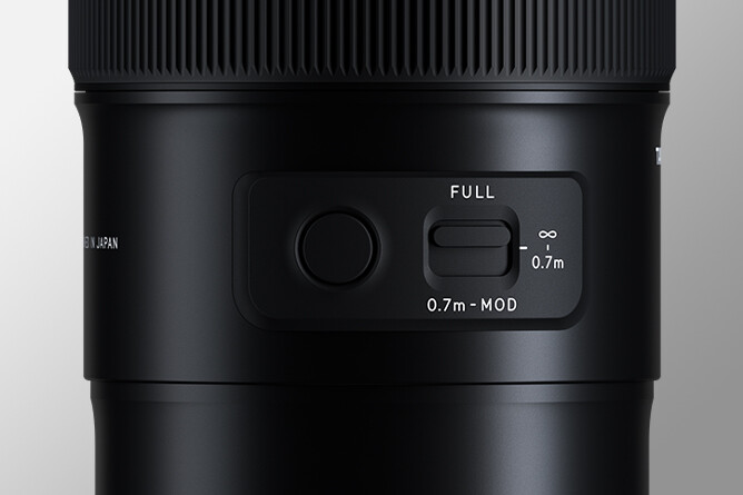 Close-up of a camera lens focus ring and distance scale markings showing minimum focus distance settings.