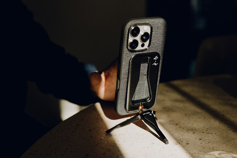 iPhone with camera case and tripod mount sitting on concrete in dramatic side lighting.