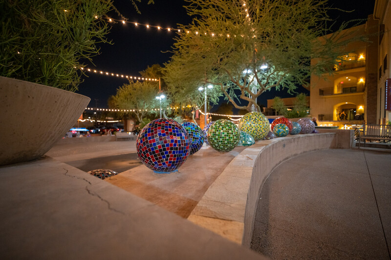 Illuminated decorative spheres with colorful geometric patterns arranged in a nighttime outdoor plaza.