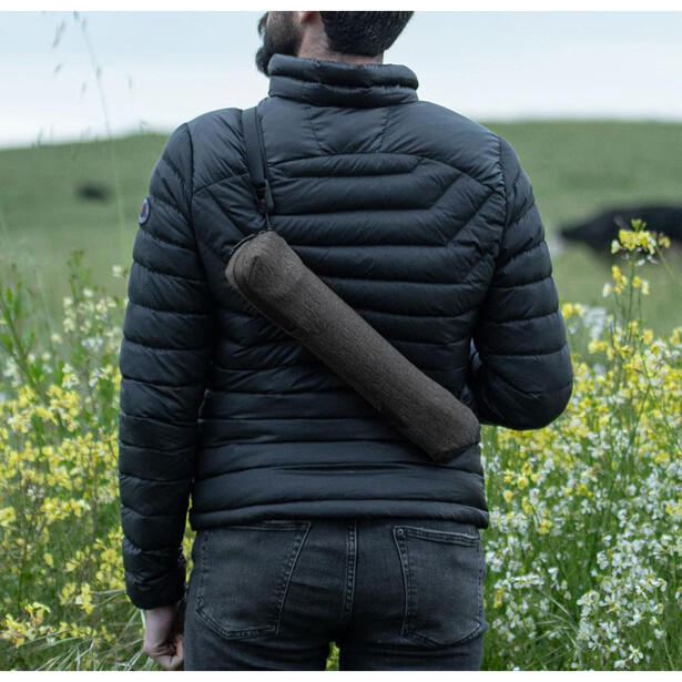 Person wearing black quilted jacket holding rolled fabric in field of yellow flowers.