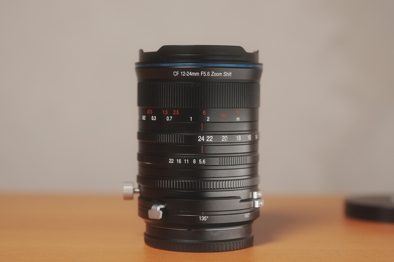 Vintage telephoto lens with multiple focus rings and depth-of-field markings displayed on wooden surface.