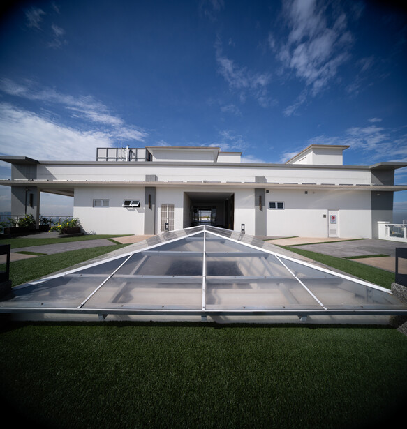 Modern white residential building with flat roof and glass pool enclosure on manicured lawn under blue sky.