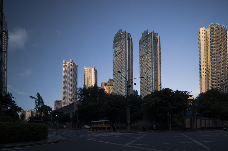 Tall residential towers lit by golden hour sunlight against a blue sky, with trees and street level visible in foreground.