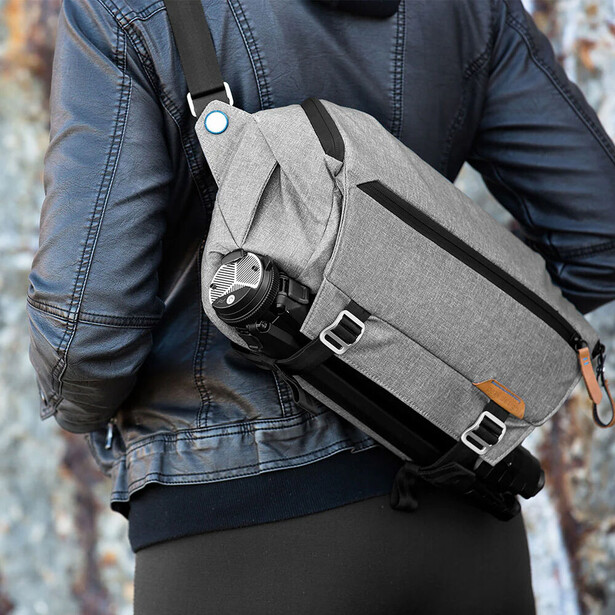 Gray camera sling bag worn over shoulder against denim jacket and dark pants.