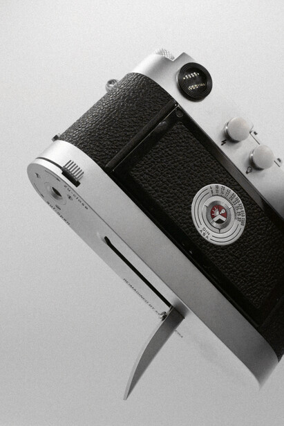 Vintage rangefinder camera with black leather body and chrome accents, displayed at an angle against white background.