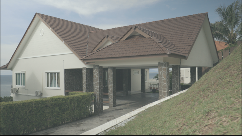 Modern residential home with white walls, brown metal roof, and stone columns supporting a covered porch area.