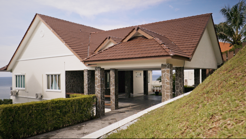 Modern residential home with white walls, terracotta tile roof, and stone columns supporting a covered porch overlooking water.