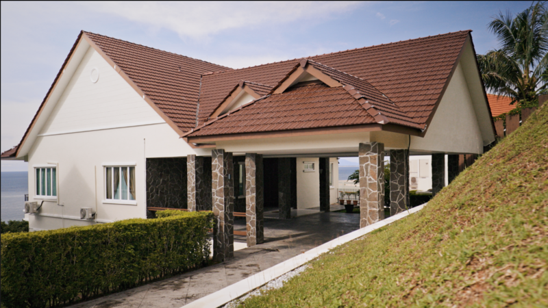 Modern residential home with white walls, brown clay tile roof, and stone columns under natural daylight.