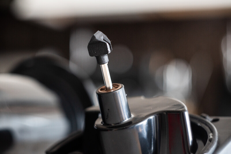Close-up of a chrome car gear shift lever with blurred interior background.