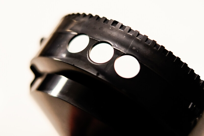 Close-up of a black camera lens barrel showing three circular aperture blade openings and textured focus ring detail.