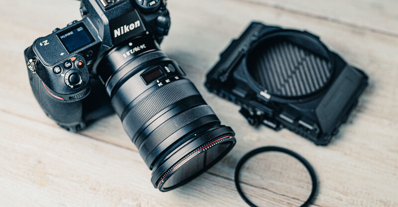 Nikon camera with attached lens, filter, and lens hood arranged on a light surface.