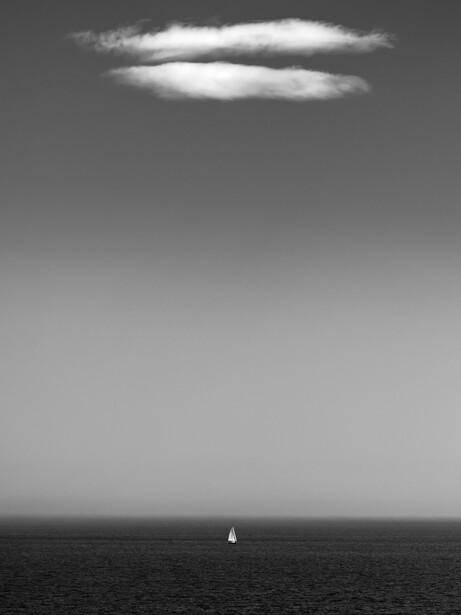 Minimalist seascape with a lone sailboat on the horizon beneath a single illuminated cloud.