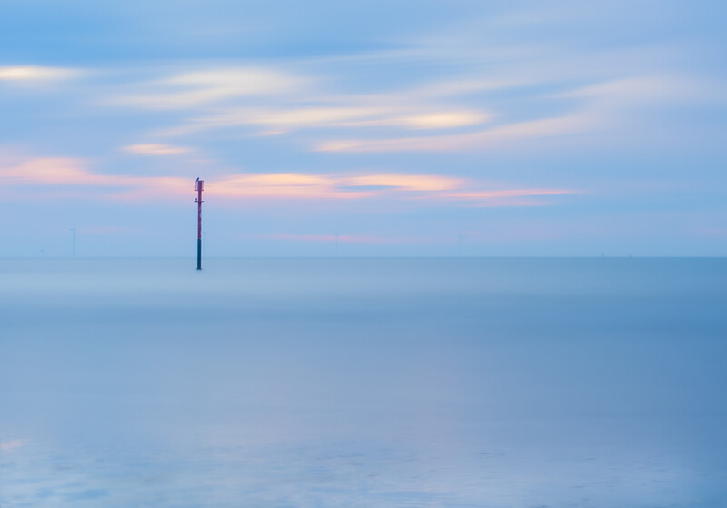 Solitary navigation buoy or marker standing in calm, flat water at dusk.