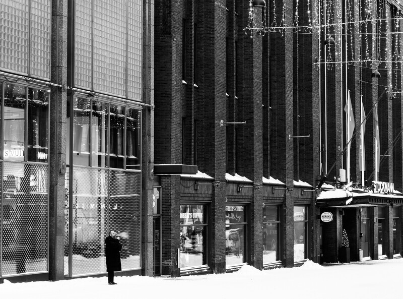 Black and white photograph of a modernist building facade with tall vertical columns and ground-level storefronts.