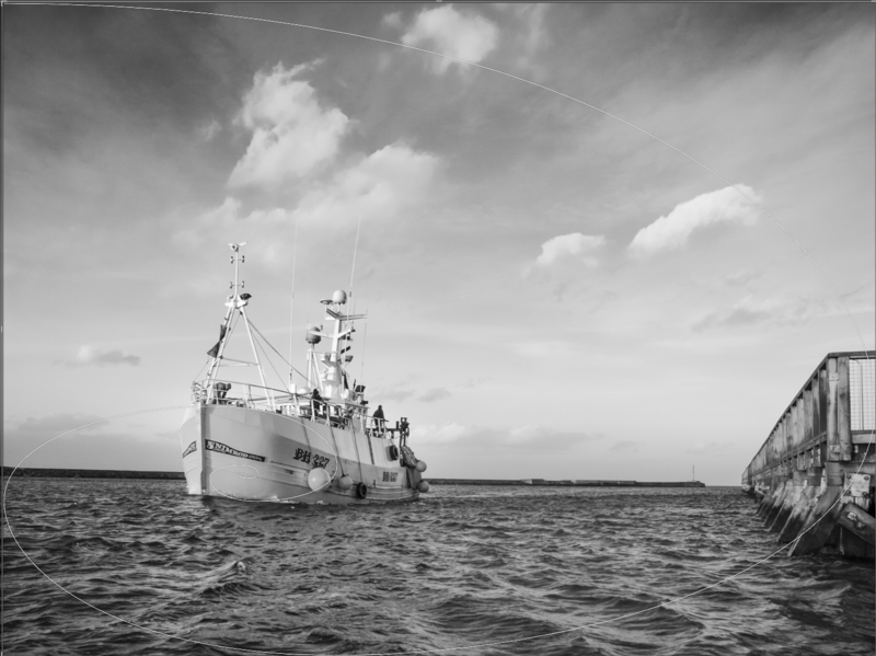 Vintage fishing vessel moored alongside a wooden pier under partly cloudy sky.