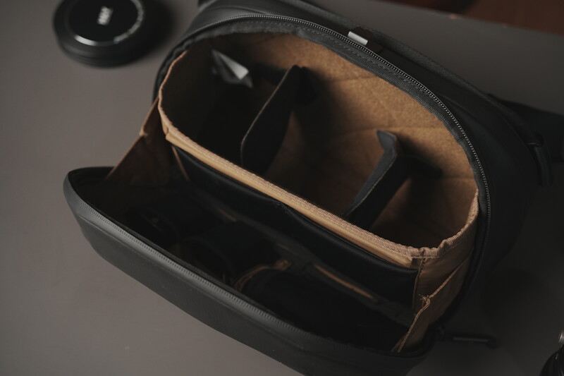 Open camera bag with brown canvas interior and black exterior compartments for gear storage.