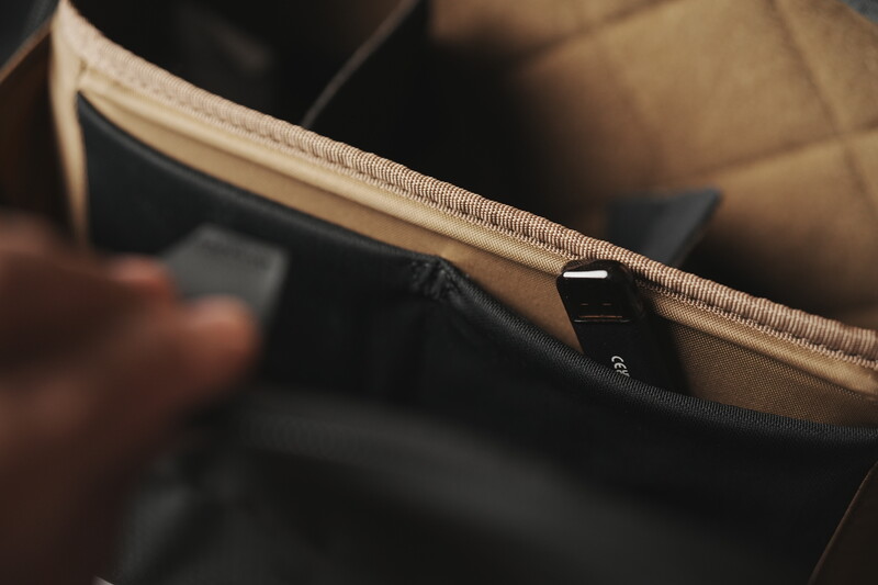 Close-up of a beige zippered pouch or bag with black fabric visible inside and a small dark tag attached.