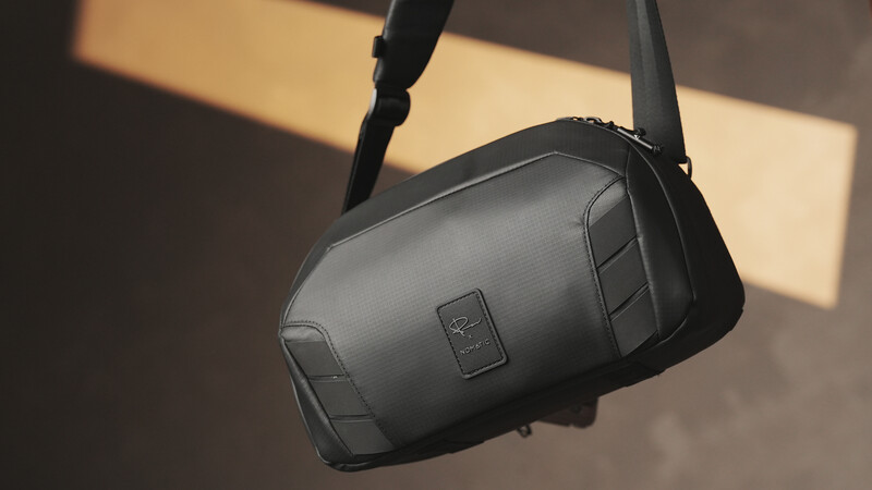 Black camera bag with shoulder strap hanging against warm interior lighting with shadows.