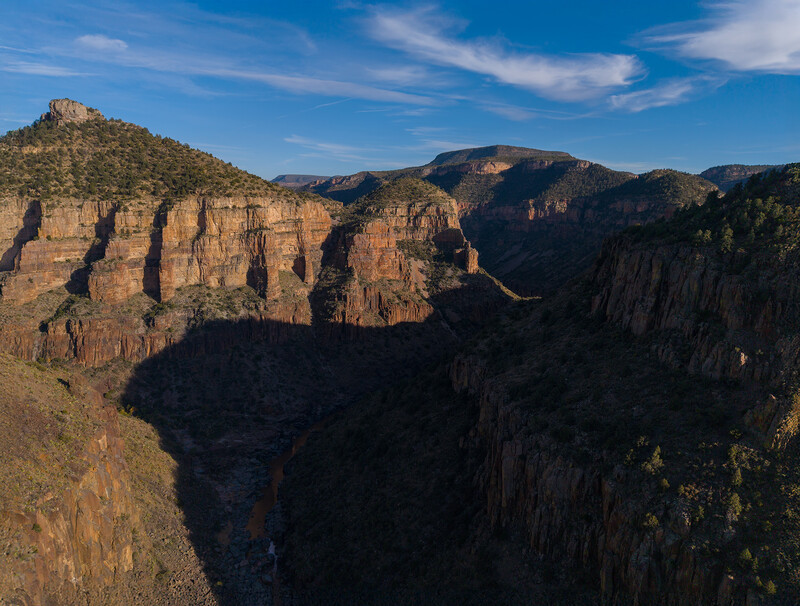 Dramatic canyon landscape with towering rock formations and deep shadows under blue sky.