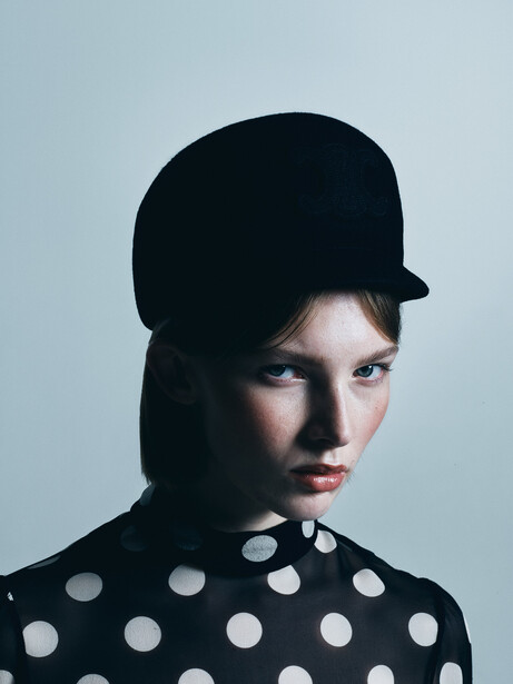 Person wearing a black cap and polka dot shirt against a neutral blue-gray background.