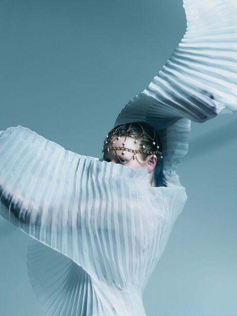 Person wearing white pleated fabric and sunglasses against clear blue sky, shot from below.