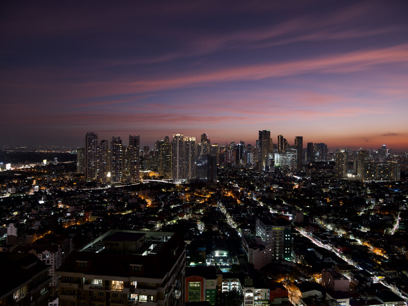 Urban skyline at dusk with illuminated buildings under purple and pink twilight sky.